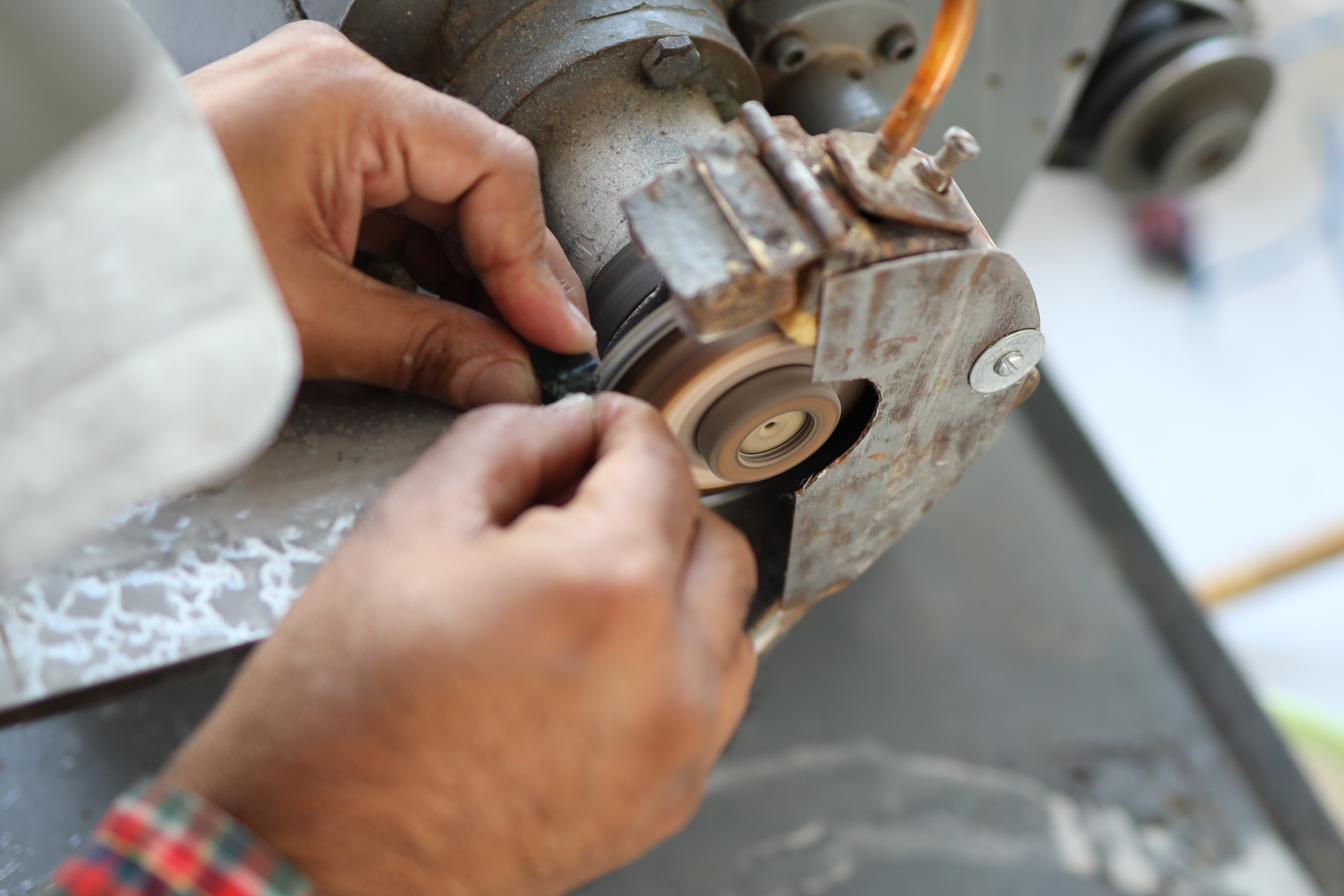 Macro view of a master cutter using a precise diamond saw to cut through a large rough emerald with sparks and water cooling